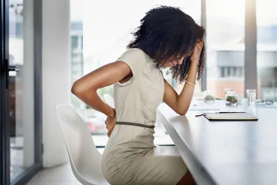 Woman at a desk holding her lower back